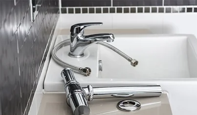 Home 4 A sink with a detached chrome faucet and hoses placed on the countertop, in front of a tiled black and white wall, indicating ongoing plumbing or faucet installation.